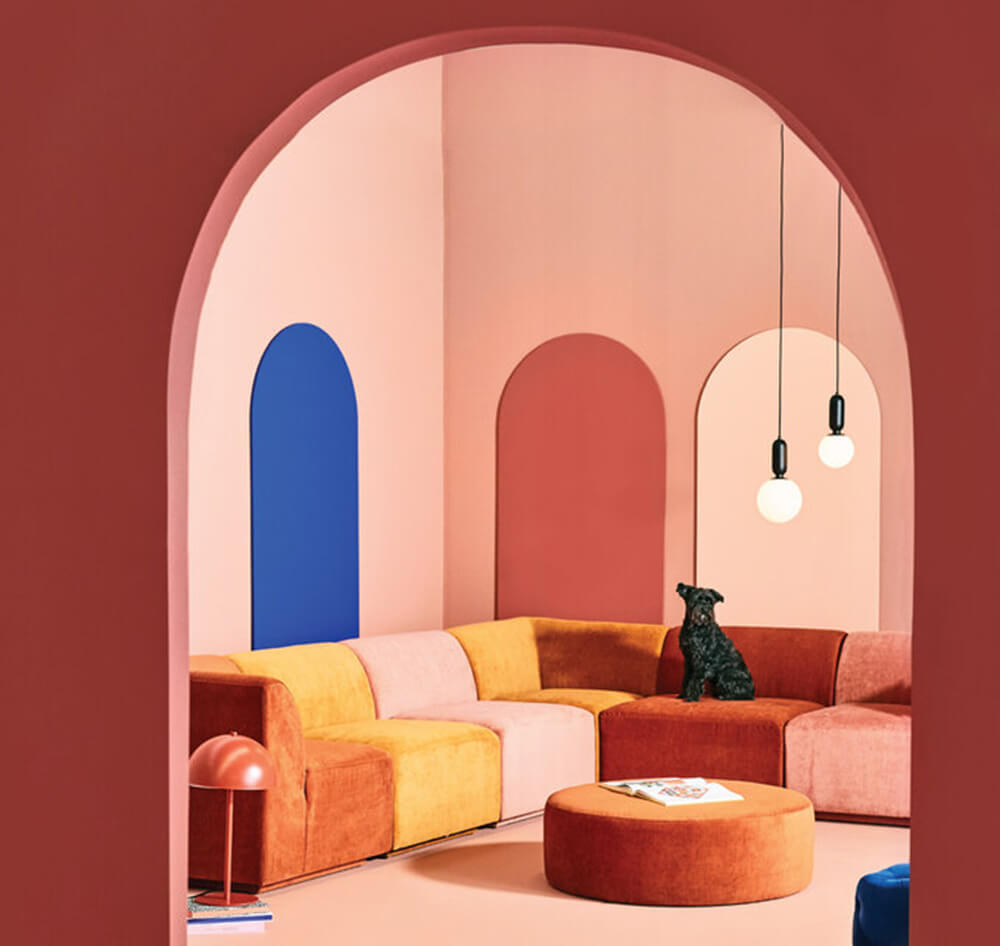 A colorful living room featuring a modular sectional in yellows, oranges, and reds, against a pink wall with blue accents.